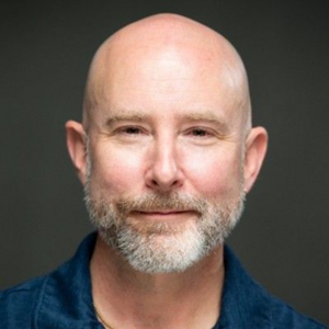 Headshot of a man with a blue collar looking into the camera.