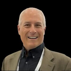 Headshot of a man in a black shirt and tan blazer.