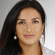 A headshot photo of Franziska Hittmair, wearing pearl earrings, and a white blouse in front of a grey background