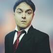 A headshot photo of Jitendra Aswani wearing a black suit jacket with a red tie in front of a blurred background